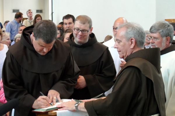 Br. Colin and Br. Michael sign the Book of Life held open by Fr. Dan Anderson, OFM
